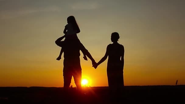 Silhouette, happy child with mother and father, family at sunset, summertime. Concept of friendly family.